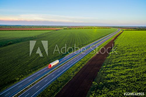 Dump trucks carrying goods on the highway. Red truck driving on asphalt road along the green fields. seen from the air. Aerial view landscape. drone photography.  cargo delivery